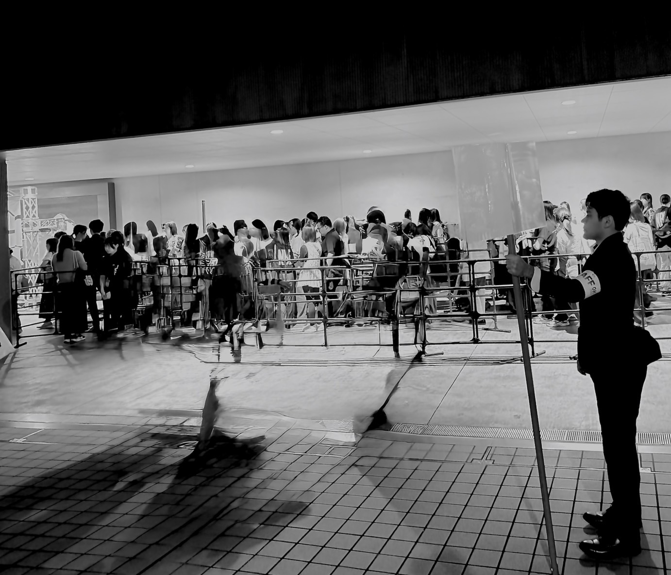 柵に沿って並ぶ大勢の来場者の横で、誘導棒を手に立つ警備員